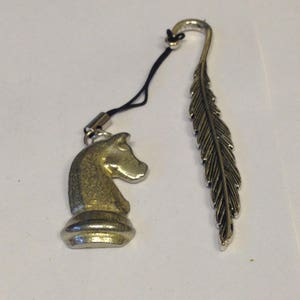 Puede incluir: Marcapáginas de plata con diseño de pluma y un dije de pieza de ajedrez de caballero de plata unido a una cuerda negra.
