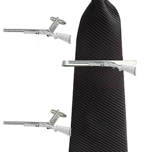 May include: A black tie with a silver shotgun tie clip and matching cufflinks. The tie clip and cufflinks are both in the shape of a shotgun.