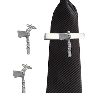May include: A set of silver-toned cufflinks and a tie bar featuring a tomahawk design. The tie bar is attached to a black tie.