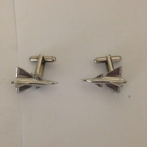 May include: A pair of silver cufflinks featuring a detailed design of a fighter jet.
