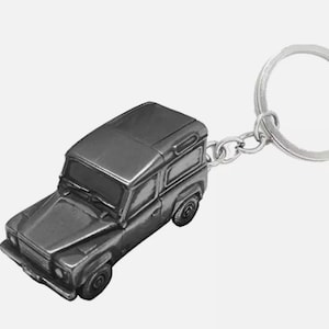 May include: A silver metal keychain featuring a detailed miniature replica of a Land Rover Defender. The keychain has a silver metal ring and chain.