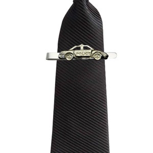 May include: A black striped tie with a silver tie clip featuring a toy police car. The car has the word "POLICE" printed on the side.