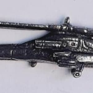 May include: A silver-toned miniature helicopter pin. The pin depicts a helicopter with a rotor and detailed body features. The pin is designed for attachment to garments or accessories.