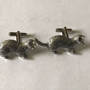 May include: A pair of silver cufflinks featuring a detailed ferret design. The cufflinks are made of metal and have a polished finish.