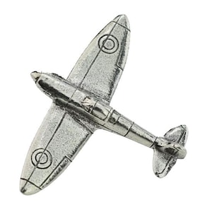 Puede incluir: Un avión en miniatura de color plateado con líneas detalladas en las alas y el fuselaje. El modelo presenta marcas circulares en las alas y un timón de cola. El avión está sobre un fondo blanco.