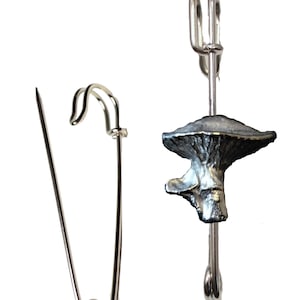 May include: A silver mushroom-shaped pin with a safety pin closure. The pin is made of metal and has a realistic mushroom design.