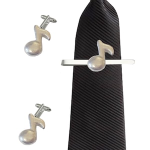 May include: A set of silver musical note cufflinks and a matching tie bar. The tie bar is attached to a black striped tie.