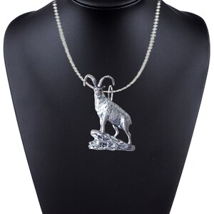 May include: A silver necklace with a pendant of a mountain goat standing on a rock. The goat is detailed with horns, hooves, and fur.