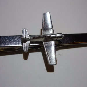 May include: Silver tie clip featuring a detailed airplane design. The airplane is in a flying position with wings spread out.