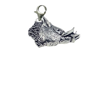 May include: A silver charm in the shape of a wild boar's head. The charm has a detailed design and is attached to a silver jump ring.