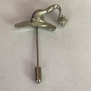 May include: Silver-toned witch hat lapel pin with a pointed hat and a curled brim. The hat has a small, curled detail on the top.