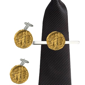 Puede incluir: Un juego de gemelos y un pasador de corbata dorados con un diseño de moneda romana. El pasador de corbata está unido a una corbata negra a rayas.