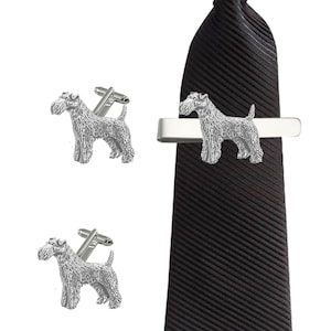 May include: A silver tie clip and cufflinks set featuring a wirehaired fox terrier dog design. The tie clip is attached to a black striped tie.