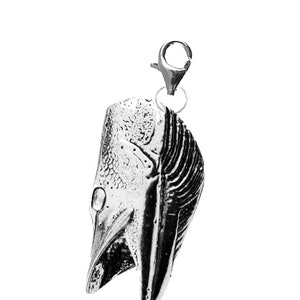 May include: A silver charm in the shape of a fish with a detailed design. The charm has a loop at the top for attaching to a necklace or bracelet.