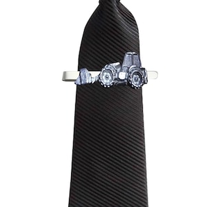 Puede incluir: Una corbata negra con un clip de corbata plateado con un diseño de tractor.