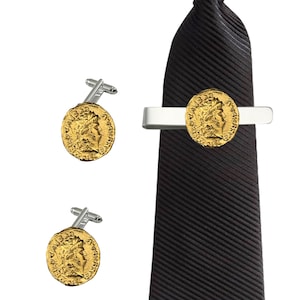 Puede incluir: Un juego de gemelos y pasador de corbata de oro con una réplica de una moneda romana. El pasador de corbata es de plata con un diseño de moneda de oro. Los gemelos son de plata con diseños de monedas de oro. El pasador de corbata y los gemelos se muestran en una corbata negra.