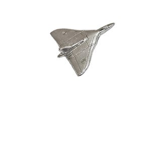 Op de afbeelding: Een zilverkleurige vliegtuigspeld met een deltavleugelontwerp. De speld heeft gedetailleerde kenmerken, waaronder kleine cirkelvormige accenten en een puntige neus. Het vliegtuig staat tegen een effen witte achtergrond.