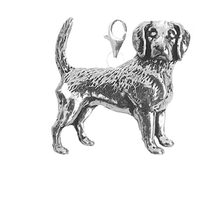 Puede incluir: Un amuleto de plata de un perro Beagle de pie con la cola enroscada. El amuleto tiene un bucle en la parte superior para sujetarlo a un collar o pulsera.