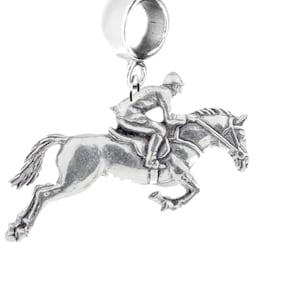 May include: Silver charm featuring a rider jumping a horse. The charm is designed to be attached to a bracelet or necklace.