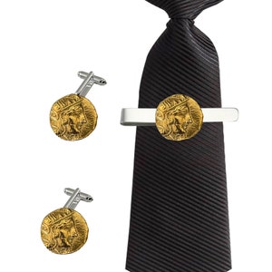 Puede incluir: Un juego de gemelos y pasador de corbata de oro con una réplica de una antigua moneda griega. El pasador de corbata es de plata y la corbata es negra.