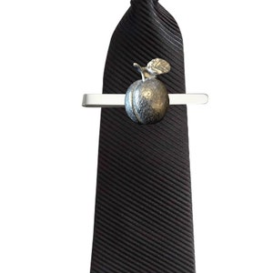 May include: A black tie with a silver tie clip featuring a sculpted peach design.