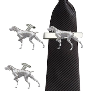 May include: A silver tie clip and cufflinks set featuring a German Shorthaired Pointer dog design. The tie clip is attached to a black tie.