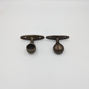 May include: Two antique gold-toned metal curtain rod finials with a round ball shape. Each finial has a flat, rectangular base with two holes for mounting.