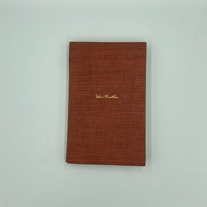 May include: A brown book with the text "John Ruskin" in gold lettering on the front cover.