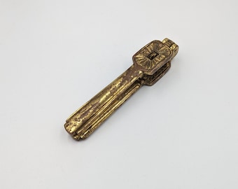 May include: A gold-toned metal nutcracker with an ornate design. The nutcracker is closed and has a detailed floral pattern on the handle.