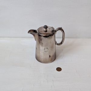 May include: A silver teapot with a round lid and a handle. The teapot has a circular design on the side with the text "The Hall Sheffield" inside the circle.