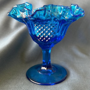 Op de afbeelding: Een levendige blauwe glazen voetbokaal met een gerimpelde rand. De bokaal heeft een ruitpatroon aan de binnenkant en een ronde voet. De steel is slank. De bokaal is waarschijnlijk vintage of antiek.