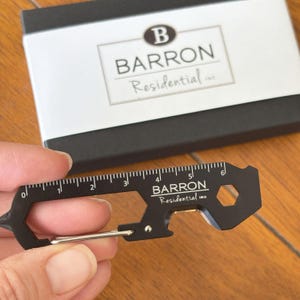 May include: Black multi-tool with a ruler, bottle opener, and carabiner clip. The tool is engraved with "BARRON Residential Inc."