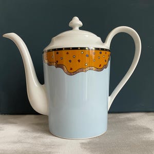 以下が含まれることがあります： ライトブルーのボディ、白い注ぎ口とハンドル、白い蓋が付いたセラミックコーヒーポット。上部には、カラフルなドットデザインと金色のトリムが付いたオレンジ色のバンドがあります。コーヒーまたは紅茶を提供するために設計されています。