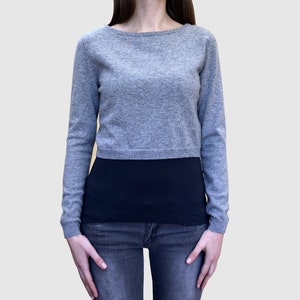 Puede incluir: Un suéter gris corto con mangas largas. El suéter está hecho de una tela suave y de punto y tiene un ajuste holgado.