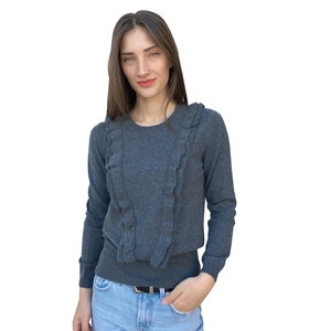 Puede incluir: Un su&eacute;ter gris de manga larga con un cuello de volantes. El su&eacute;ter est&aacute; hecho de una tela suave y de punto y tiene un ajuste holgado.