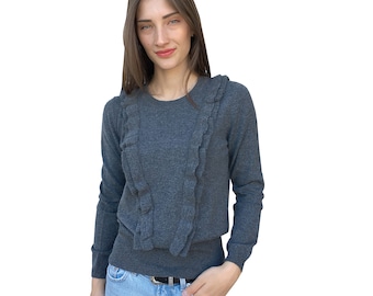 May include: A gray long-sleeved sweater with a ruffled neckline. The sweater is made of a soft, knit fabric and has a relaxed fit.