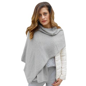 Puede incluir: Una estola de cachemira gris con cuello de tortuga. La estola está drapeada sobre los hombros de una persona y se lleva con una chaqueta blanca y pantalones grises.