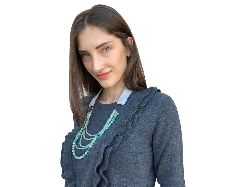 Puede incluir: Una mujer con un su&eacute;ter gris con volantes y un collar de cuentas verdes y blancas de varias capas.