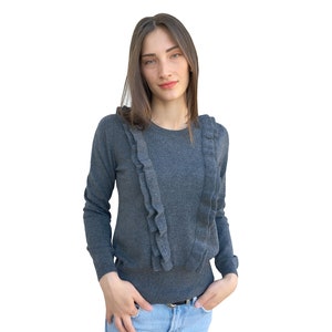 Puede incluir: Un su&eacute;ter gris de manga larga con un cuello de volantes. El su&eacute;ter est&aacute; hecho de una tela suave y de punto.