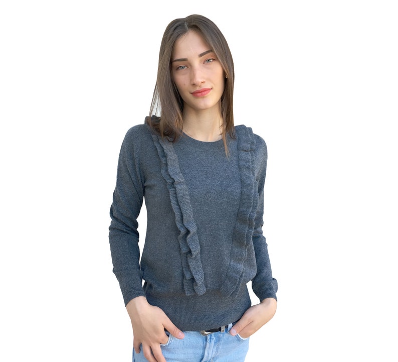 Puede incluir: Un su&eacute;ter gris de manga larga con un cuello de volantes. El su&eacute;ter est&aacute; hecho de una tela suave y de punto.