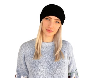 May include: A woman with long blonde hair wearing a black beanie and a light gray sweater with floral embroidery on the sleeves.