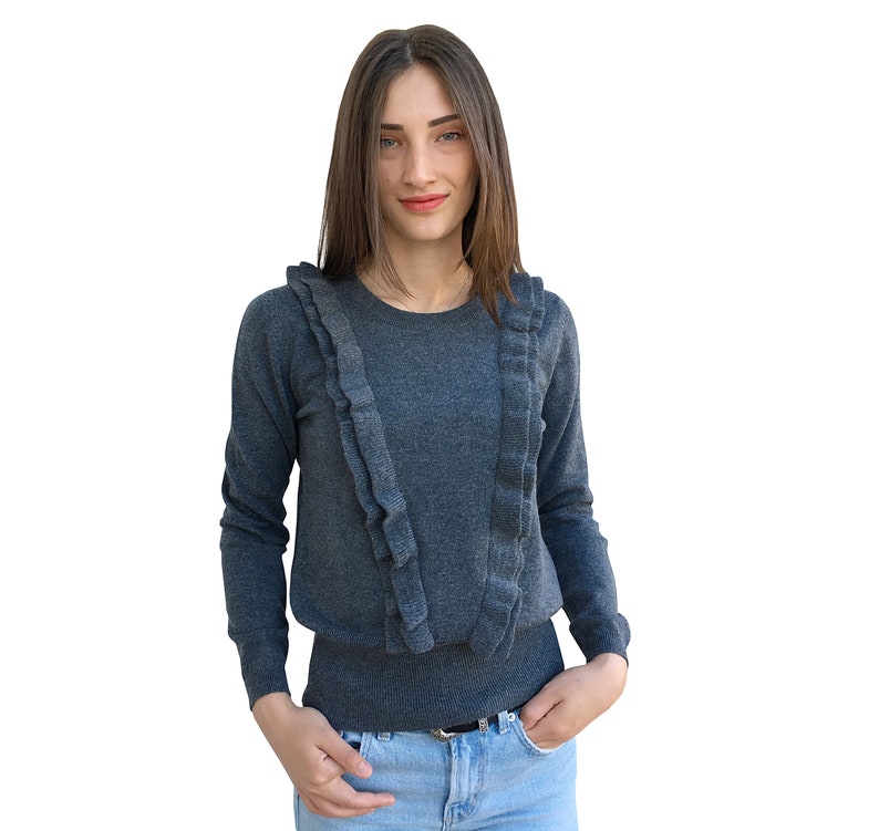 Puede incluir: Un su&eacute;ter gris de manga larga con un cuello de volantes. El su&eacute;ter est&aacute; hecho de una tela suave y de punto.