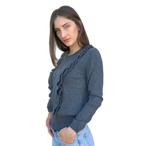 Puede incluir: Una mujer con un su&eacute;ter gris con un detalle de volantes y jeans azules.