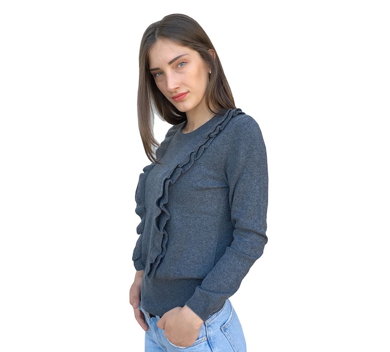 Puede incluir: Una mujer con un su&eacute;ter gris con un detalle de volantes y jeans azules.