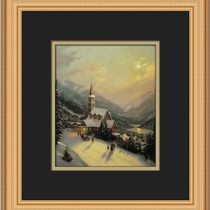 May include: A framed landscape painting depicts a snow-covered village nestled in a valley, with a church as the focal point. The artwork features a warm color palette, with a golden frame and a black matting.