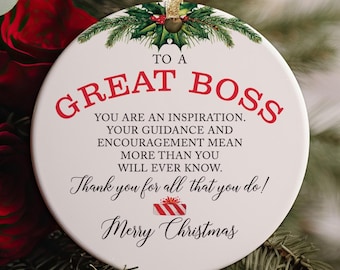 May include: A round white ceramic ornament featuring a gold ribbon hanger and a holly sprig graphic at the top. The text reads: TO A GREAT BOSS, YOU ARE AN INSPIRATION. YOUR GUIDANCE AND ENCOURAGEMENT MEAN MORE THAN YOU WILL EVER KNOW. Thank you for all that you do! Merry Christmas, with a small red and white striped gift box icon.
