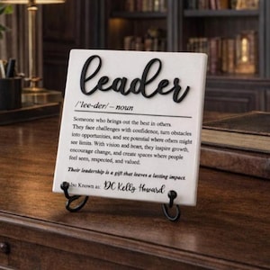 May include: A white square plaque with black text featuring the word leader, its phonetic spelling, and a definition. The text describes a leader as someone who brings out the best in others. The plaque includes the name DC Kelly Howard at the bottom.