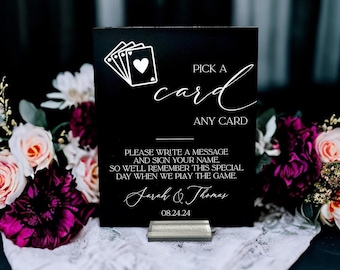 Könnte beinhalten: Ein rechteckiges schwarzes Schild mit weißem Text und einer Spielkartengrafik. Der Text lautet: PICK A card ANY CARD, PLEASE WRITE A MESSAGE AND SIGN YOUR NAME, SO WE'LL REMEMBER THIS SPECIAL DAY WHEN WE PLAY THE GAME. Sarah & Thomas 24.08.24.