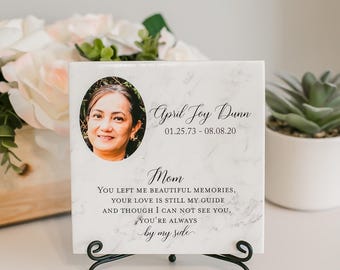Könnte beinhalten: Eine quadratische Gedenktafel mit weißem Marmormuster, einem ovalen Foto einer Frau, dem Namen April Joy Dunn, den Daten 01.25.73 - 08.08.20 und dem Text Mom You left me beautiful memories, your love is still my guide.