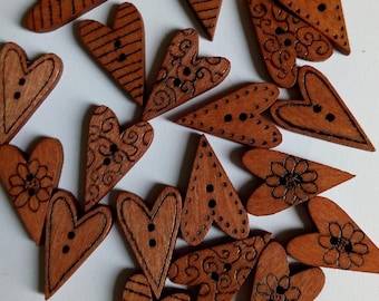 May include: A collection of wooden heart-shaped buttons with various designs, including swirls, flowers, and stripes. The buttons are brown and have two holes each.